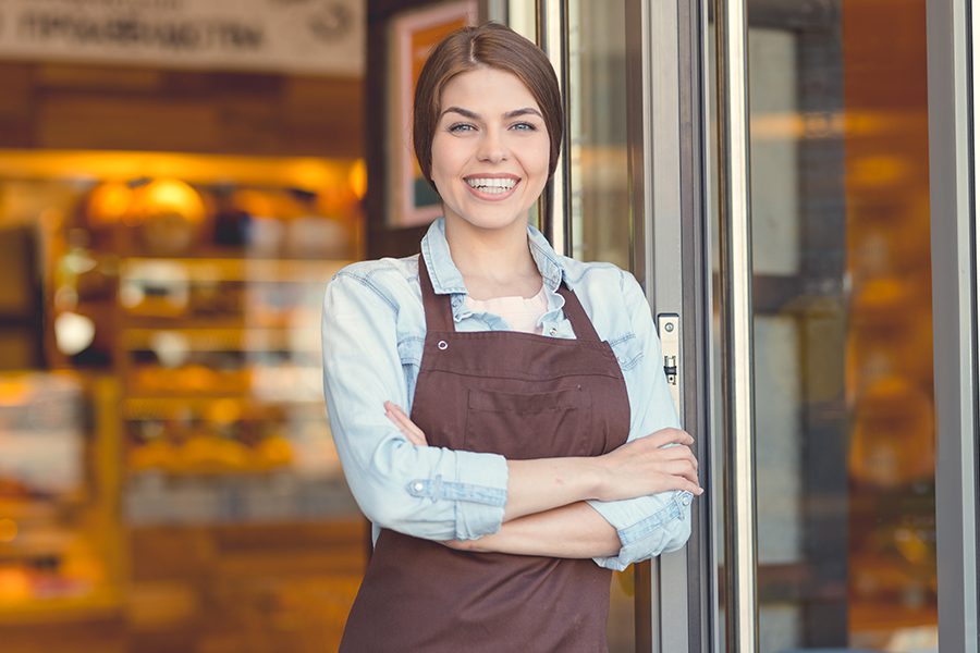 Business Insurance - Smiling Business Owner in Uniform in Front of Her Bakery