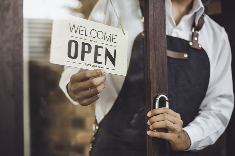 Business Owners Insurance - Store Owner Turning Open Sign Through the Glass Door and is Ready for Service